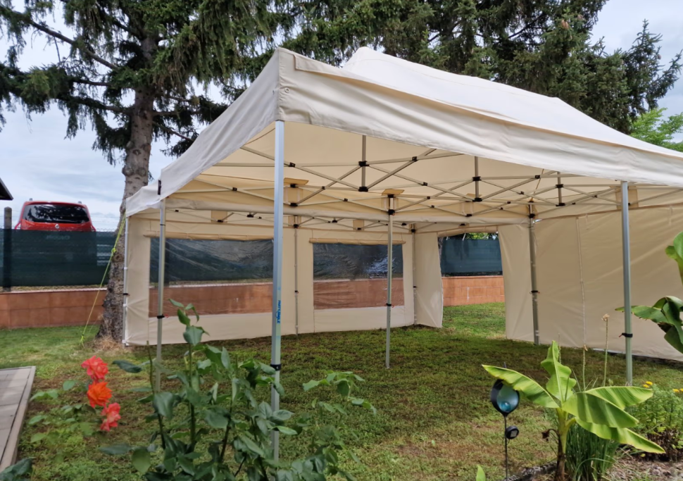 Zelt in einem Garten mit geöffneten Seiten und grüner Vegetation im Vordergrund.