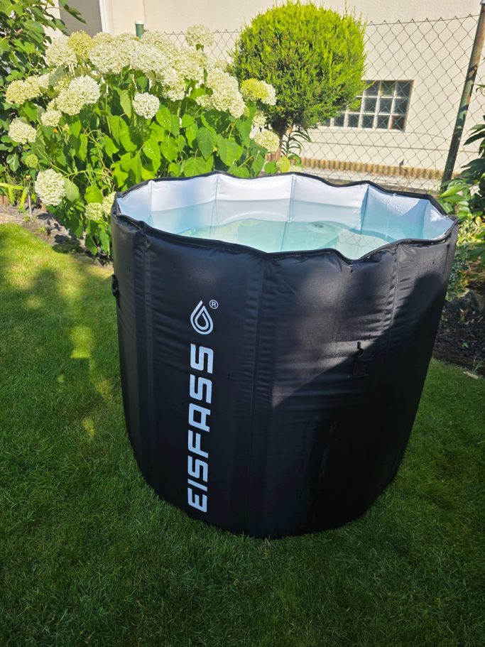 Schwarz-weißer aufblasbarer Pool im Garten, umgeben von grünen Pflanzen und Blumen.