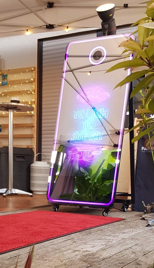 Ein moderner Fotobox-Spiegel mit bunten Lichtern und Pflanzen im Hintergrund.