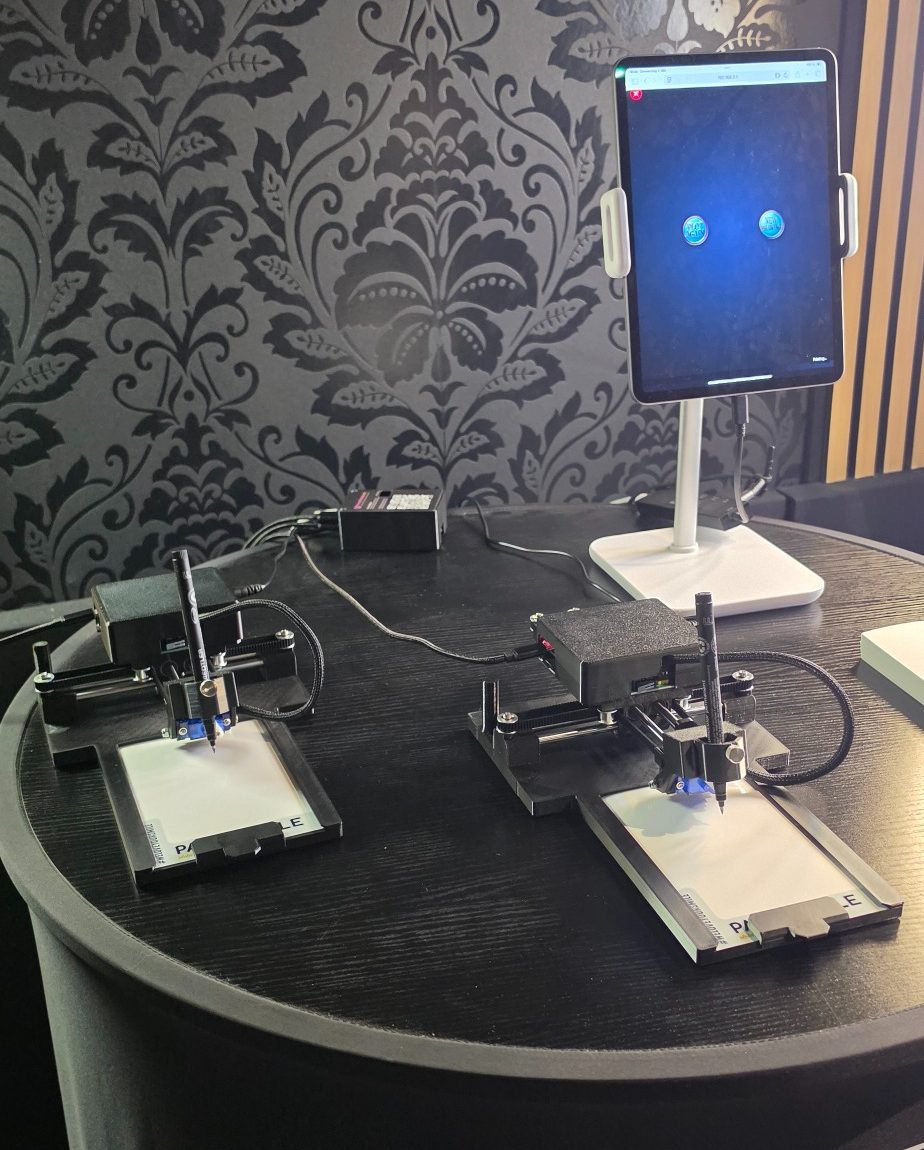 Zwei Sketcharo-Zeichenroboter mit Tablet auf dem optionalen runden Tisch Zwei Sketcharo-Zeichenroboter mit Tablet auf dem optionalen runden Tisch